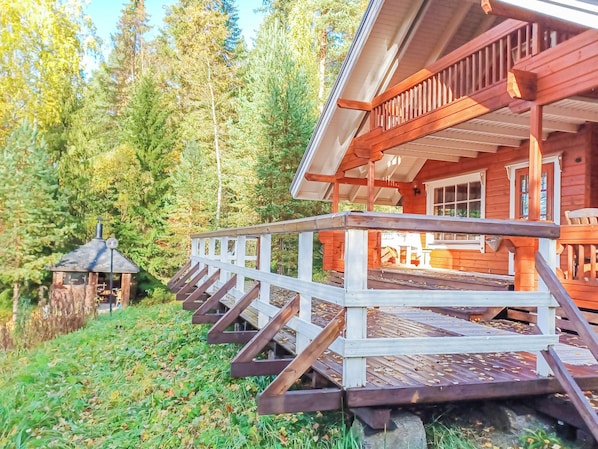 A wooden cabin with a porch and a small shed in a forested area.