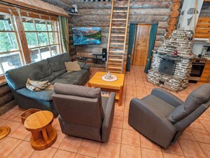 A log cabin interior with a sofa, armchairs, a table, a fireplace, a TV, and a ladder. - Luminalle by Interhome (Kuusamo)