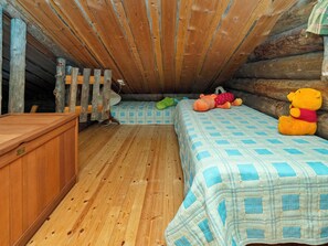 Um quarto de sótão acolhedor com piso de madeira, uma cama com colcha xadrez azul e branco, cômoda de madeira e um brinquedo de pelúcia.