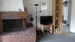Ein Wohnzimmer mit Kamin aus Backstein, einem Fernseher, einer Stehlampe und einem Bücherregal aus Holz.