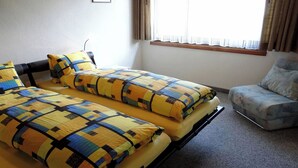 Ein Zimmer mit zwei Betten, einem Sessel und einem Fenster mit Vorhängen.