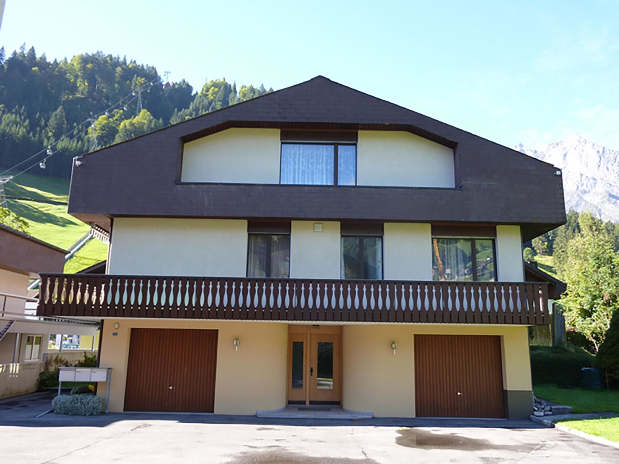 Un bâtiment à deux étages doté d’un balcon, de deux portes de garage et ayant une chaîne de montagnes en toile de fond.