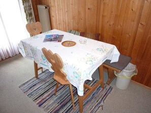 A dining table with a floral tablecloth, wooden chairs, and a small rug on the floor.