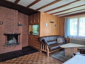 A cozy living room with a fireplace, a leather sofa, a wooden table, and a kitchen area. - Steinacher Appartement/Fewo 5-Bettwohnung by Interhome (Engelberg)