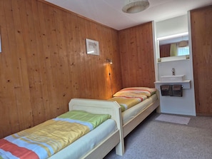 A room with two single beds, a small bathroom with a sink, and a mirror above the sink. - Steinacher Appartement/Fewo 5-Bettwohnung by Interhome (Engelberg)