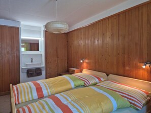 Une chambre avec deux lits, un mur en bois, un petit lavabo et un luminaire suspendu.