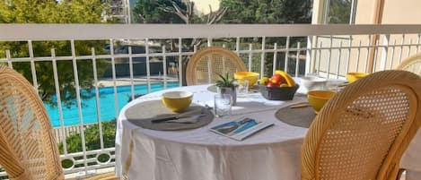 A round table with a white tablecloth, wicker chairs, and a view of a swimming pool.