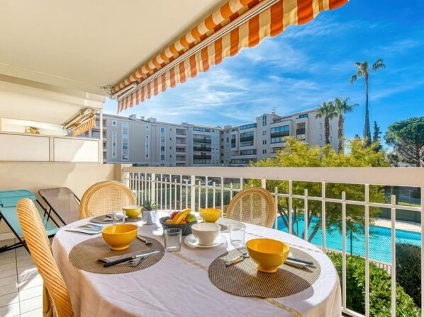 A balcony with a table set for dining, overlooking a swimming pool and a building complex.