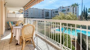 En balkon med udsigt over en swimmingpool, et spiseområde med fletstole og et gelænder med stribet stof.