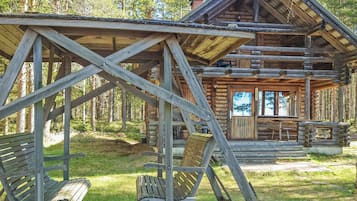 Una cabaña rústica de troncos con un porche, bancos de madera y vistas despejadas del bosque circundante.