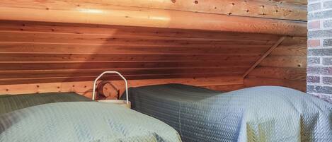 A small, cozy room with two single beds, a wooden ceiling, and a brick wall.