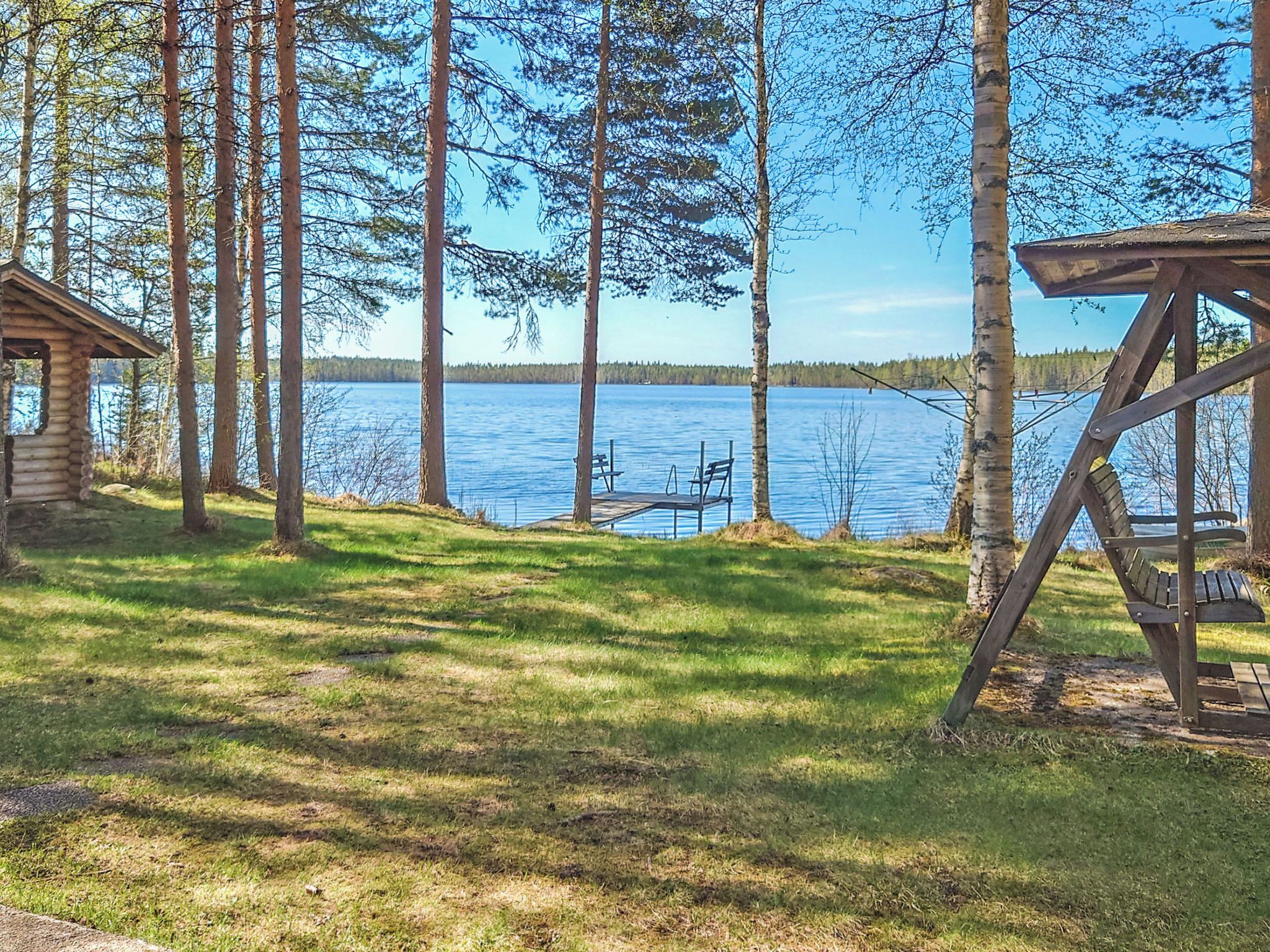 Mökki, jonka laiturilta on kulku järveen, ja jonka ympärillä on puita.