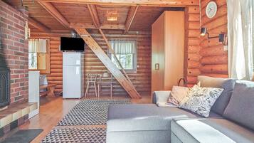 A cozy cabin interior with a living room, kitchen, and a staircase leading to an upper level.