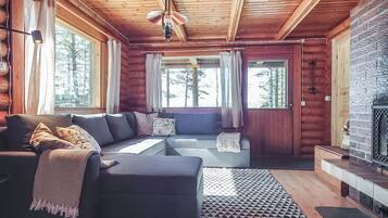 A log cabin interior with a sectional sofa, a fireplace, and large windows.
