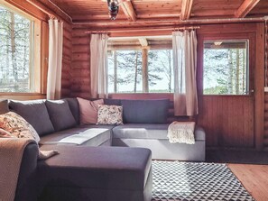 A log cabin interior with a sectional sofa, a small table, and a patterned rug. - Haapala by Interhome (Soini)
