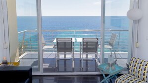Een balkon met een glazen deur, twee stoelen, een klein tafeltje en een gestreept bankje.