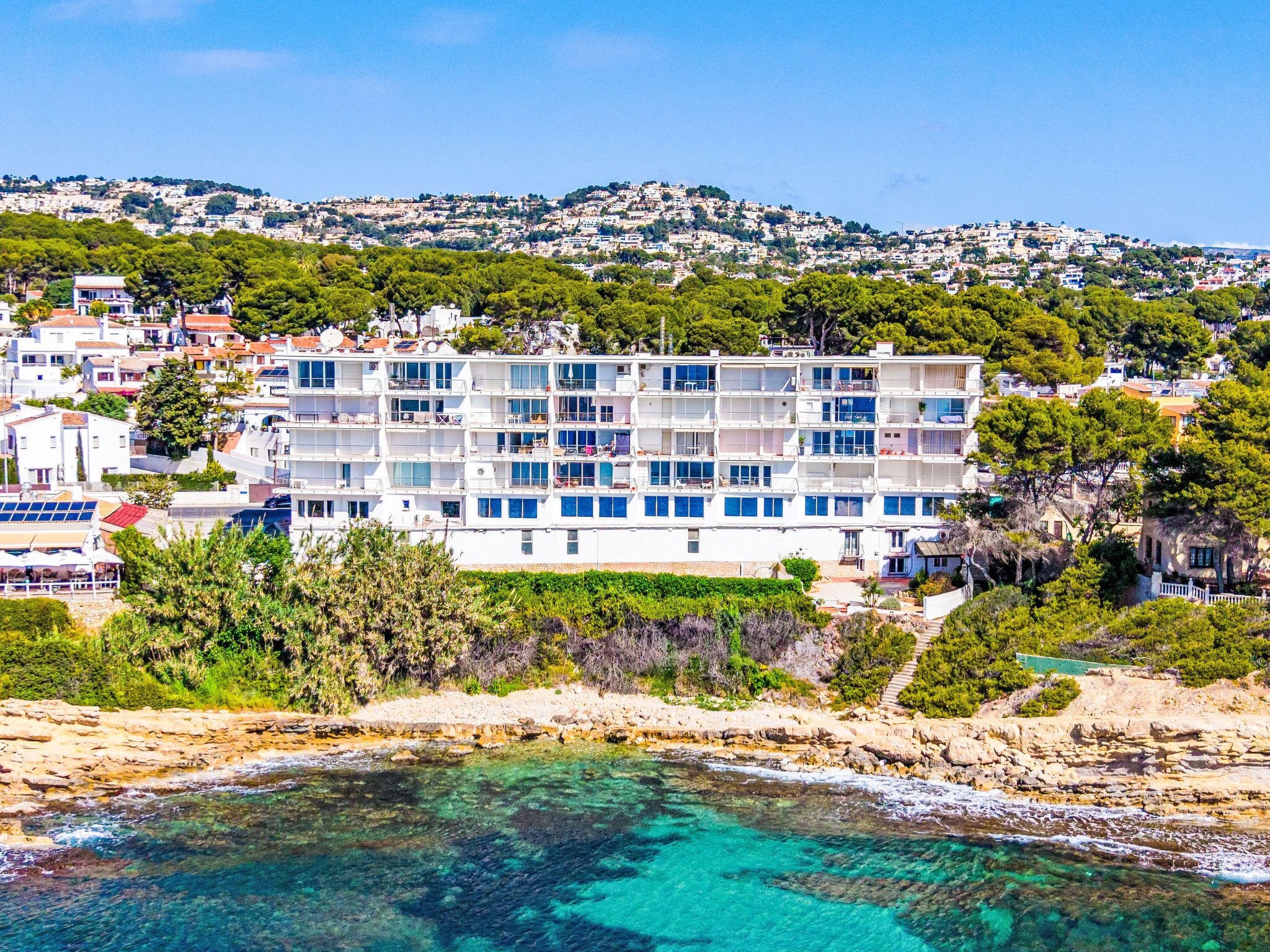 A coastal hotel with multiple floors, balconies, and a view of the sea.