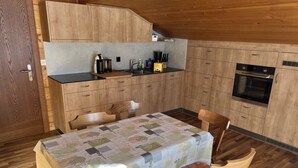 A compact kitchen with wooden cabinets, a built-in oven, and a dining area with a table and chairs. - Weideli by Interhome (Saas-Grund)