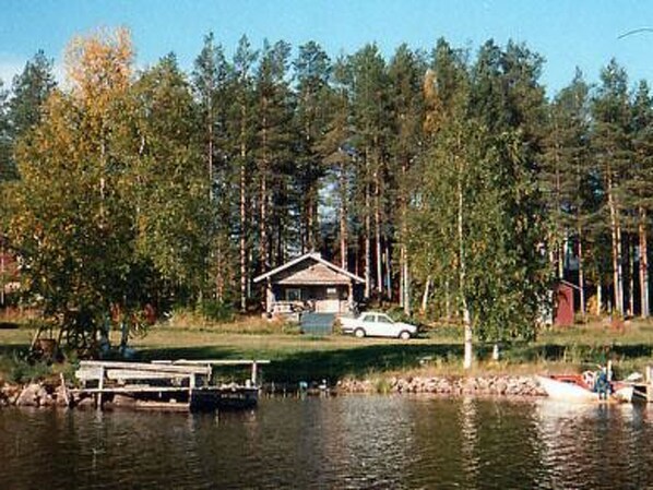 A cabin by a lake with a dock, surrounded by tall trees.