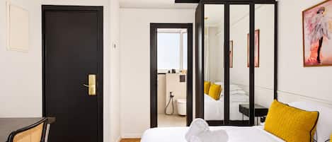 A hotel room with a bed, a desk, a chair, a bathroom, and a mirror.