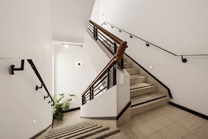 Una escalera moderna con barandilla de madera y pasamanos de metal negro, que conduce a una plataforma con una planta en maceta.