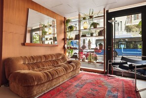 A room with a brown sofa, a large mirror, a bookshelf with plants, and a view of the street through a glass door. - Theodor Rothschild Tel-Aviv (Tel Aviv)