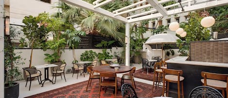 Eine Terrassengruppe mit Tischen und Stühlen, umgeben von Kübelpflanzen und einer Pergola.