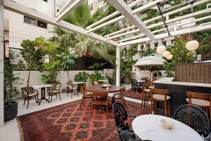 Un patio exterior con mesas y sillas, rodeado de plantas en macetas y una estructura de pérgola.