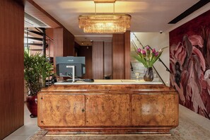 A reception desk with a flat-screen monitor, a potted plant, and a wall with a floral mural. - Theodor Rothschild Tel-Aviv (Tel Aviv)