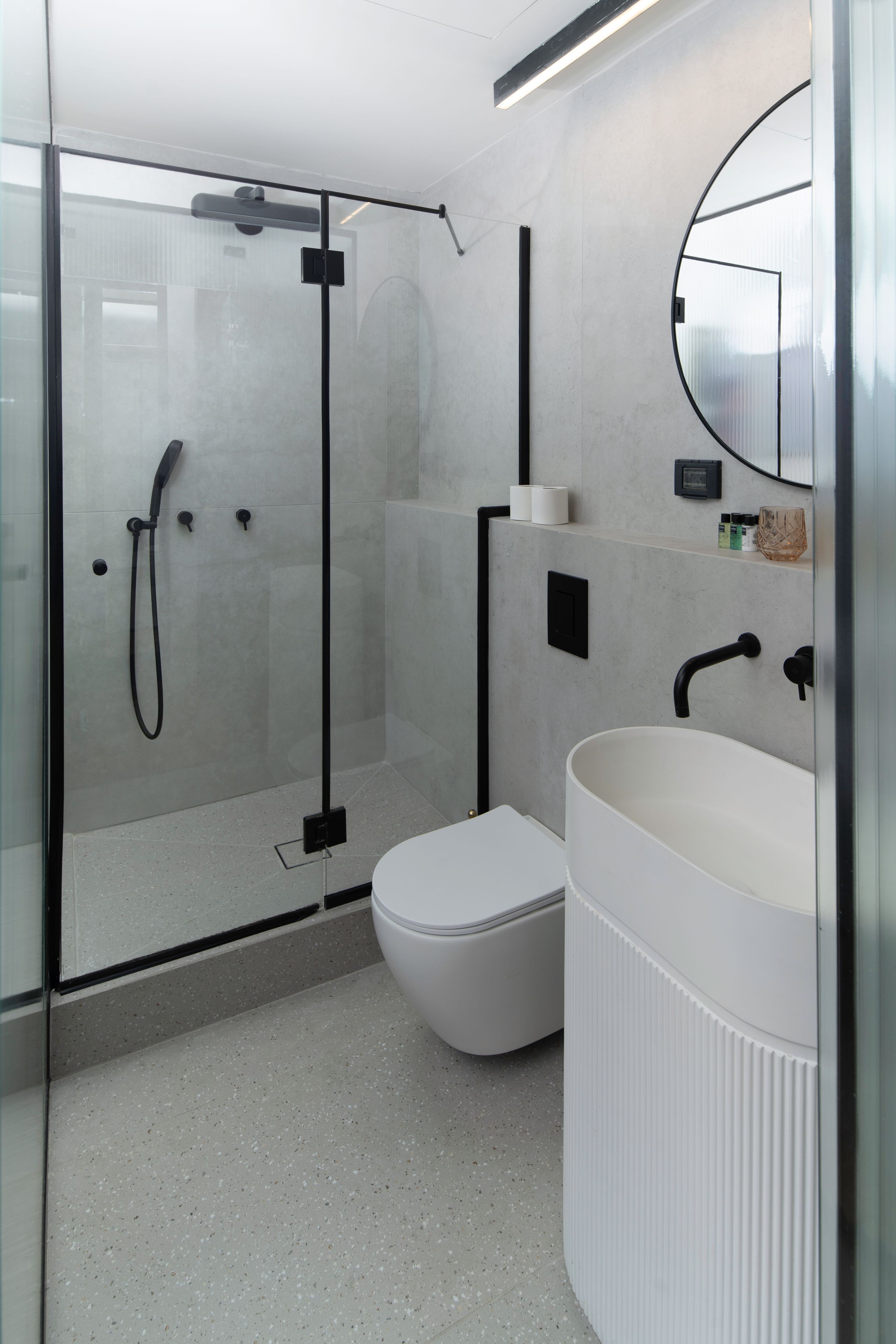 Ein modernes Badezimmer mit einer Duschkabine, einer weißen Toilette und einem großen Waschbecken mit Spiegel.