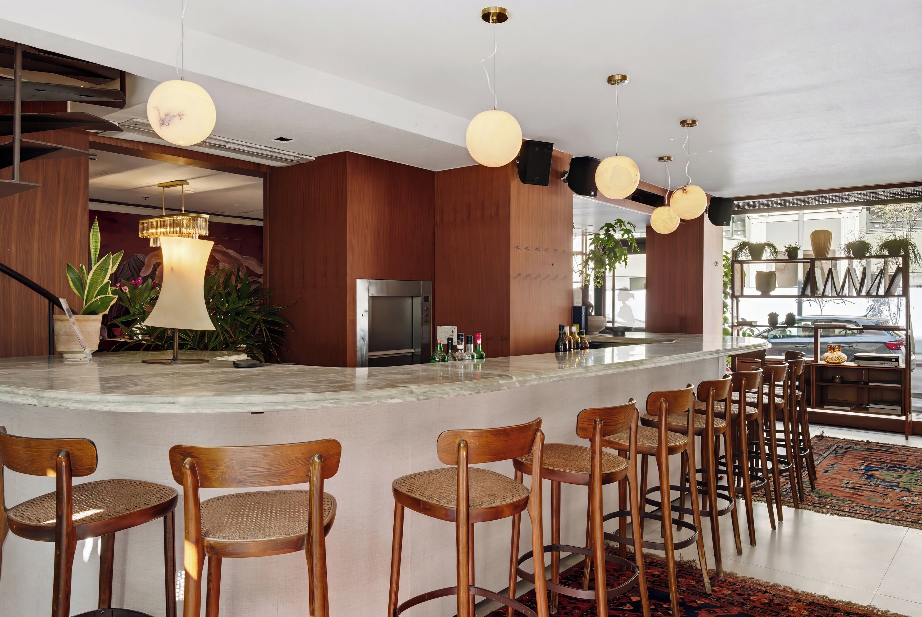A modern bar area with wooden chairs, a marble countertop, and pendant lighting.