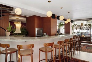 Un'area bar moderna con sedie in legno, un bancone in marmo e illuminazione a sospensione.