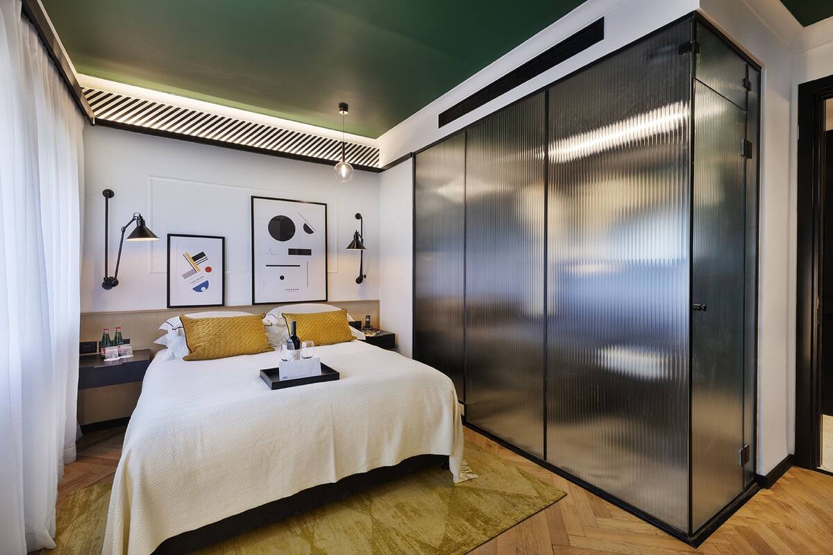 A modern hotel room with a large bed, a wardrobe, and a desk with a lamp.