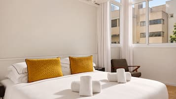 A hotel room with a large bed, two pillows, a chair, and a window with a view of buildings.