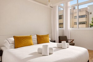 Una camera d'albergo con un letto grande, due cuscini, una sedia e una finestra con vista sugli edifici.