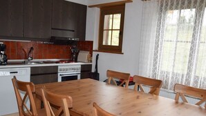 Eine Küche mit Holztisch und -stühlen, einem Herd und einem Fenster mit Vorhängen.