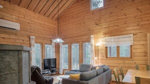 Interior acogedor de una cabaña con sofá, televisión, mesa de comedor y chimenea.