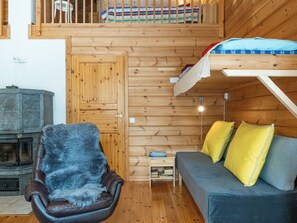 Un intérieur de chalet chaleureux avec un plancher en bois, un canapé agrémenté de coussins jaunes, un fauteuil en cuir avec un plaid en fourrure et un lit superposé recouvert d’une couverture colorée.