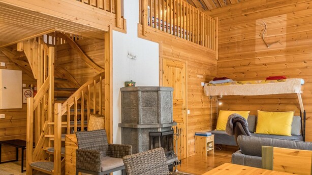 Un interior de cabaña acogedor con una escalera de madera, chimenea, sofá y literas.