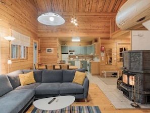 Un intérieur de chalet chaleureux avec un canapé, une table à manger, un coin cuisine et une cheminée.