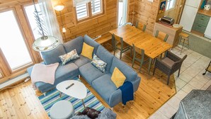 Un interior de cabaña acogedor, con un sofá azul, una mesa de comedor de madera y una zona de cocina.