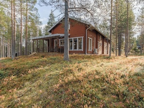 Une cabane en rondins avec un porche, entourée d’une forêt.