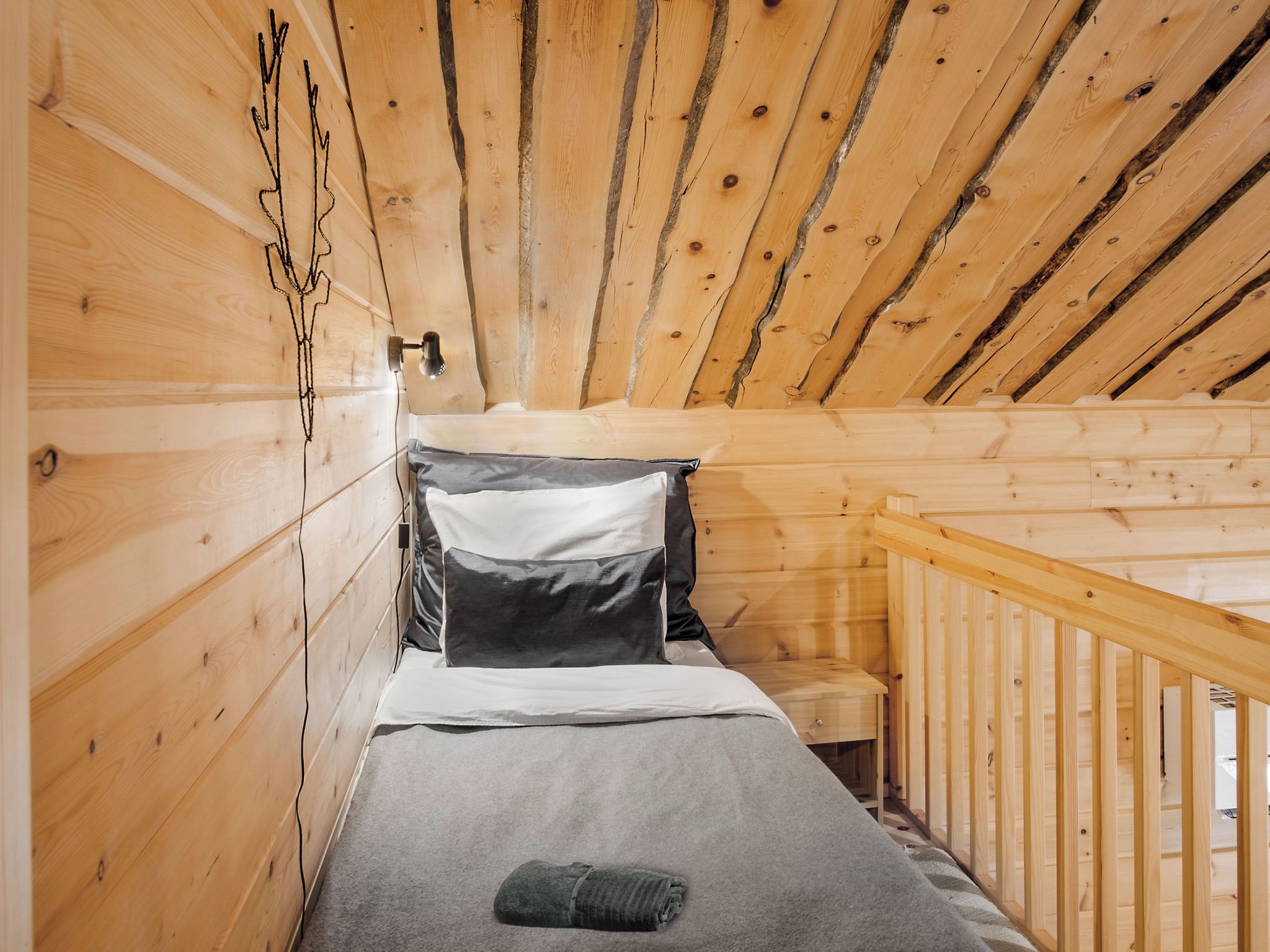 Une chambre dans un chalet en bois, avec un lit superposé, une petite table de chevet et une rambarde en bois.