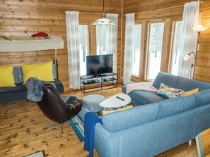 L’intérieur d’un chalet chaleureux, avec un canapé, un fauteuil et un téléviseur posé sur un meuble.