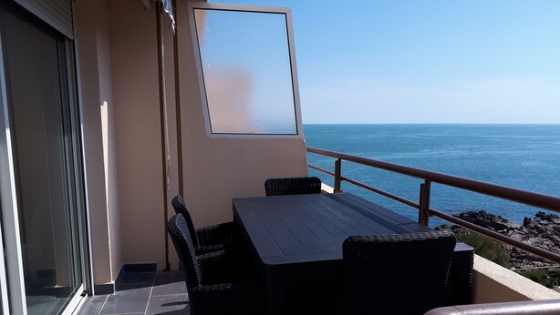 A balcony with a table and chairs, a sliding glass door, and a view of the ocean. - T2 air-conditioned sea view, WIFI, swimming pool and parking (Sète)