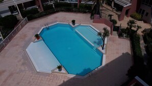 An outdoor swimming pool surrounded by a tiled patio, with palm trees and a building in the background. - T2 air-conditioned sea view, WIFI, swimming pool and parking (Sète)