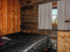 Una habitación tipo cabaña de troncos con una cama, un aparador de madera y una ventana con cortinas.