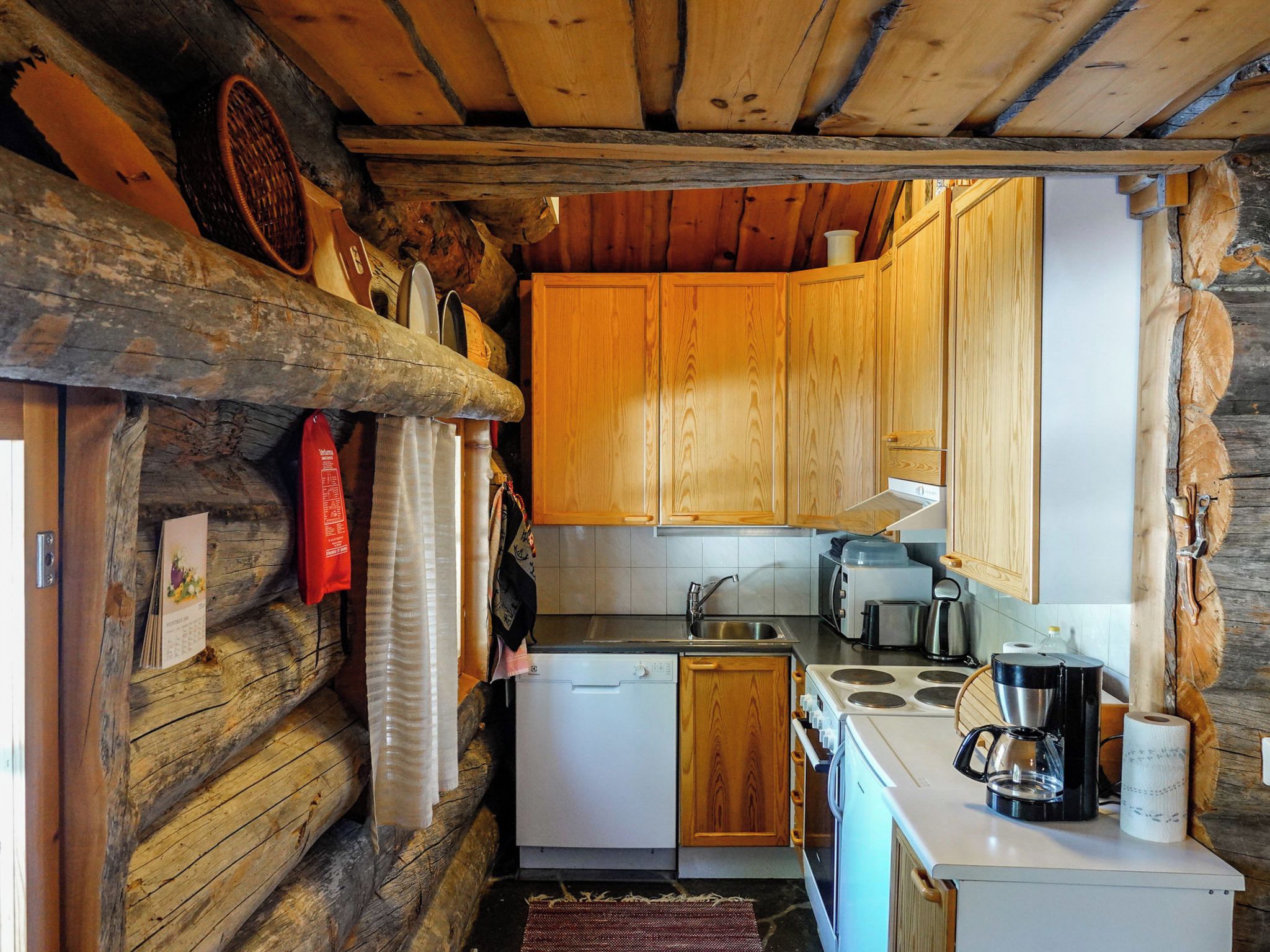 Une cuisine compacte avec des meubles en bois, un lave-vaisselle blanc, une cuisinière et une machine à café.