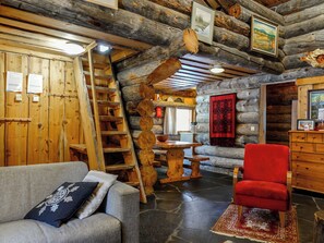 A log cabin interior with a stone floor, wooden furniture, a red armchair, a wooden ladder, and a fireplace. - Kelo-ville by Interhome (Sodankylä)