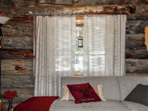 Interior de una cabaña de troncos con una cama, una ventana con cortinas y un techo rústico de madera.